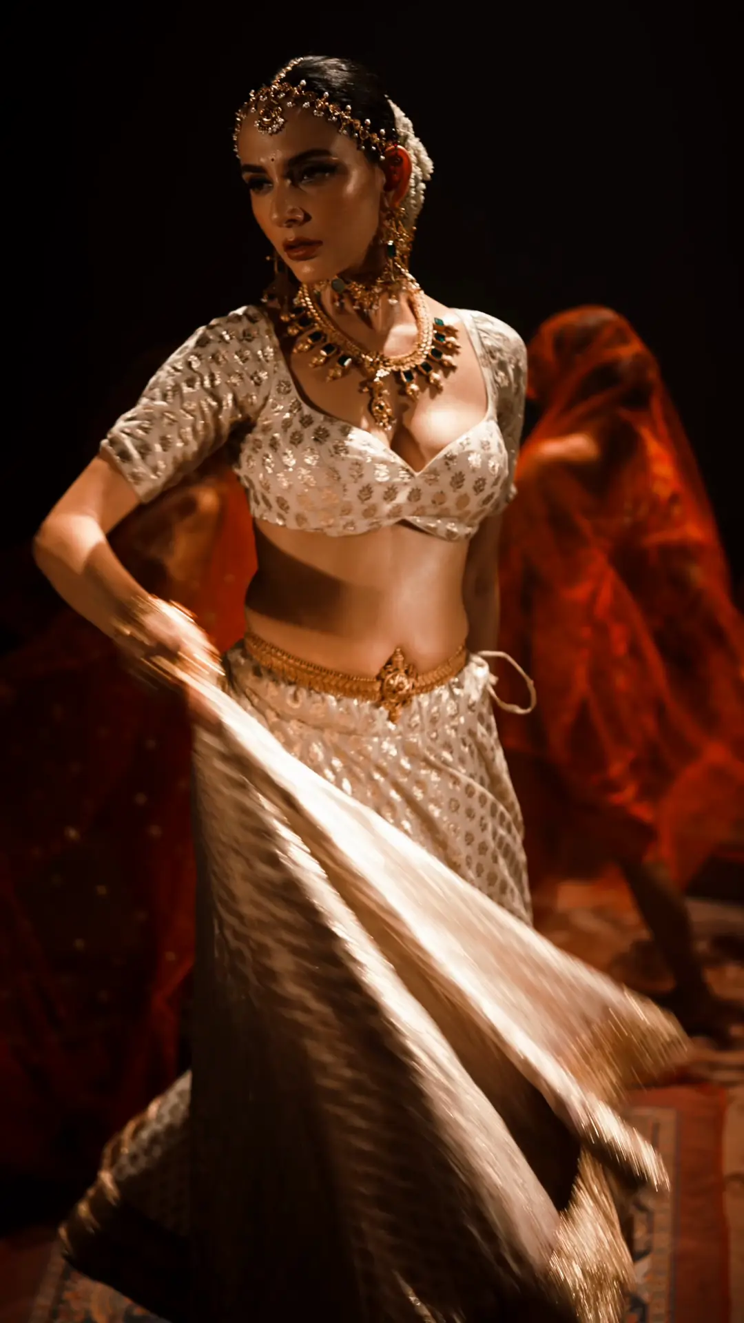 A silver-gold lehenga skirt flares mid-turn against a deep red dupatta